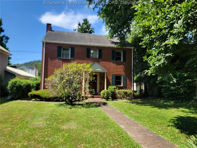 colonial home with a chimney, brick siding, and a front yard