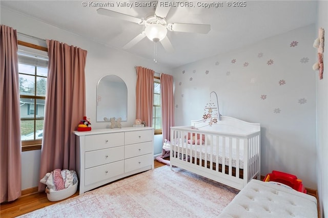 bedroom with ceiling fan, light hardwood / wood-style flooring, and a nursery area