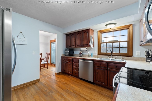 kitchen featuring appliances with stainless steel finishes, dark brown cabinets, a textured ceiling, sink, and light hardwood / wood-style floors