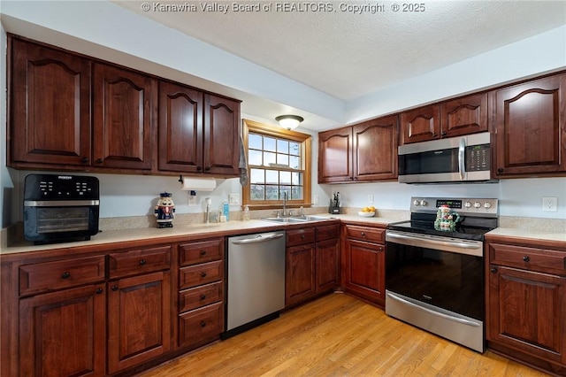 kitchen featuring sink, light hardwood / wood-style floors, a textured ceiling, and appliances with stainless steel finishes