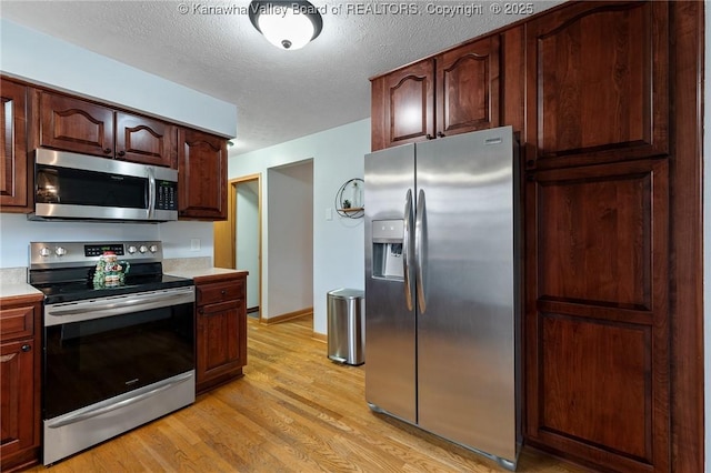 kitchen with a textured ceiling, appliances with stainless steel finishes, and light hardwood / wood-style flooring