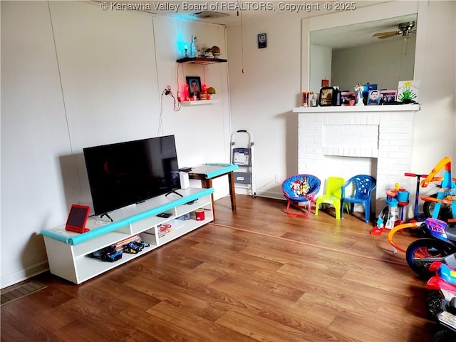 rec room with hardwood / wood-style flooring, ceiling fan, and a brick fireplace