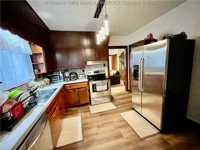 kitchen featuring stainless steel appliances, an inviting chandelier, tasteful backsplash, light hardwood / wood-style floors, and decorative light fixtures