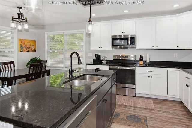 kitchen with dark stone counters, stainless steel appliances, sink, white cabinets, and hanging light fixtures