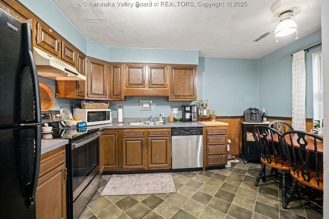 kitchen with appliances with stainless steel finishes, a textured ceiling, wooden walls, and sink