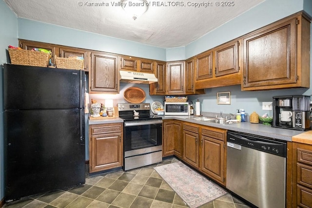 kitchen featuring a textured ceiling, sink, appliances with stainless steel finishes, and dark tile patterned flooring