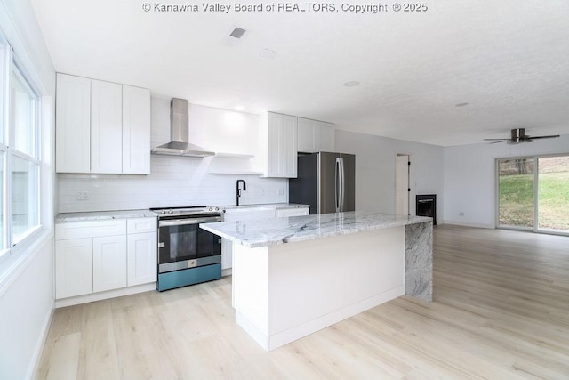 kitchen with appliances with stainless steel finishes, wall chimney exhaust hood, sink, white cabinets, and a kitchen island