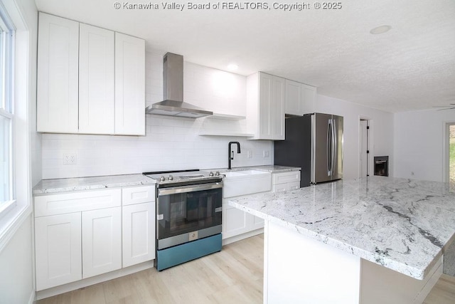 kitchen featuring white cabinets, wall chimney range hood, sink, decorative backsplash, and appliances with stainless steel finishes