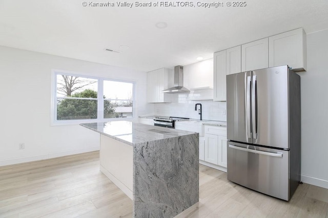 kitchen featuring light stone countertops, white cabinetry, stainless steel appliances, wall chimney range hood, and a kitchen island