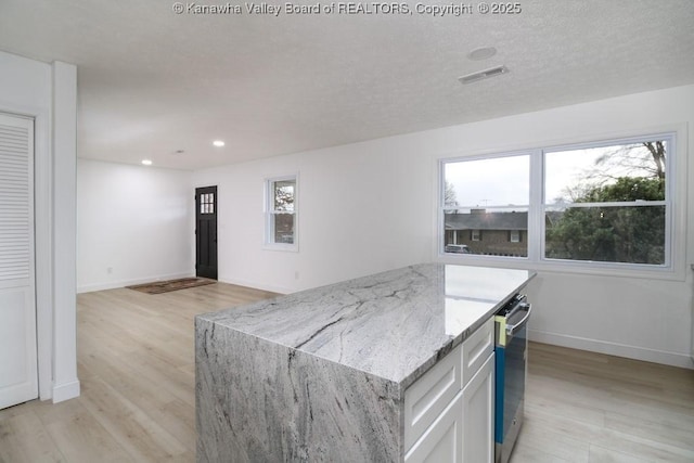 kitchen with white cabinets, a kitchen island, light stone countertops, and light hardwood / wood-style floors