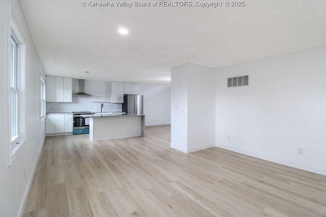 kitchen featuring white cabinetry, wall chimney range hood, tasteful backsplash, light hardwood / wood-style floors, and appliances with stainless steel finishes