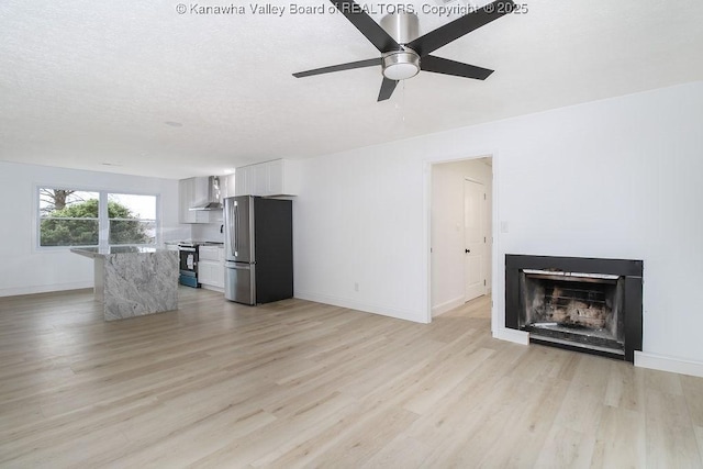 unfurnished living room featuring a textured ceiling, light wood-type flooring, and ceiling fan