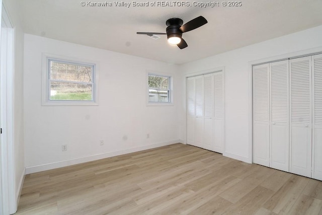 unfurnished bedroom with ceiling fan, light hardwood / wood-style floors, and multiple closets