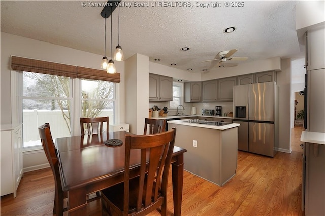 kitchen featuring stainless steel fridge, ceiling fan, sink, a center island, and hanging light fixtures