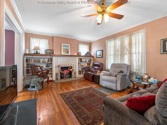 living room featuring hardwood / wood-style flooring, ceiling fan, ornamental molding, and a tile fireplace