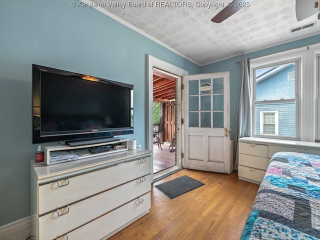 bedroom featuring ceiling fan, light hardwood / wood-style floors, a textured ceiling, and ornamental molding