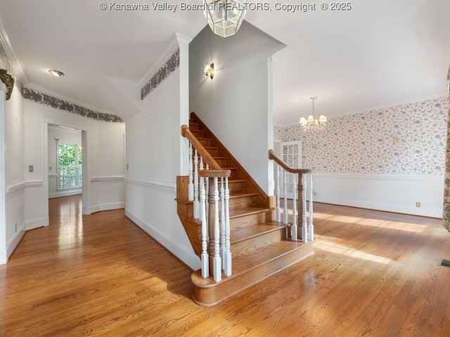 staircase featuring hardwood / wood-style flooring, ornamental molding, and an inviting chandelier