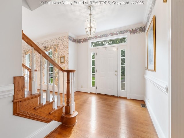 entrance foyer with light hardwood / wood-style floors, crown molding, and an inviting chandelier