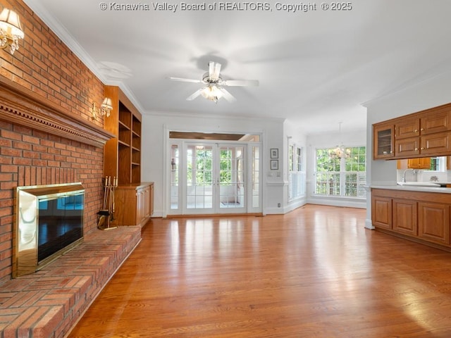 unfurnished living room featuring a wealth of natural light, crown molding, a fireplace, and ceiling fan with notable chandelier