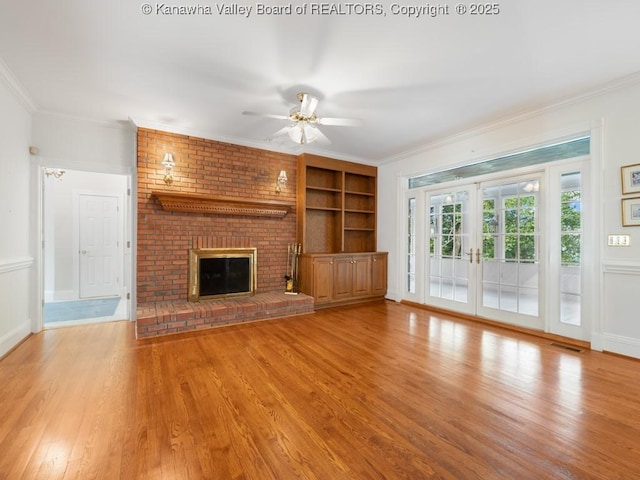 unfurnished living room featuring ceiling fan, french doors, a brick fireplace, light hardwood / wood-style flooring, and crown molding