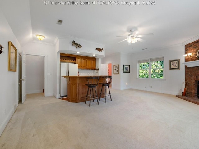 kitchen featuring crown molding, white fridge, a kitchen bar, light carpet, and a fireplace