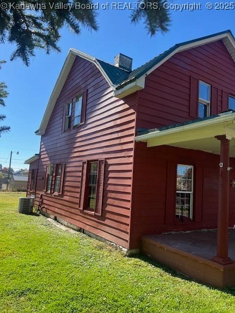 view of side of property with a lawn, covered porch, and central AC