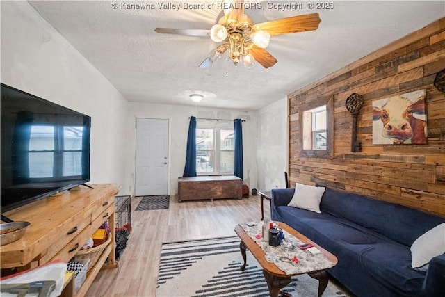 living room with a textured ceiling, light hardwood / wood-style flooring, ceiling fan, and wood walls