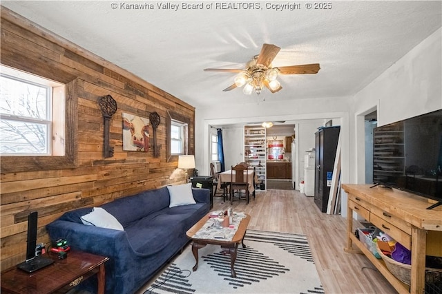 living room featuring wood walls, light hardwood / wood-style flooring, ceiling fan, and a textured ceiling