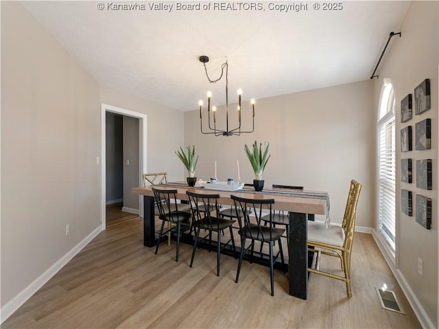 dining area with light wood-type flooring and an inviting chandelier