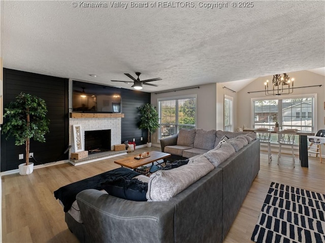 living room featuring a textured ceiling, ceiling fan with notable chandelier, a brick fireplace, and plenty of natural light