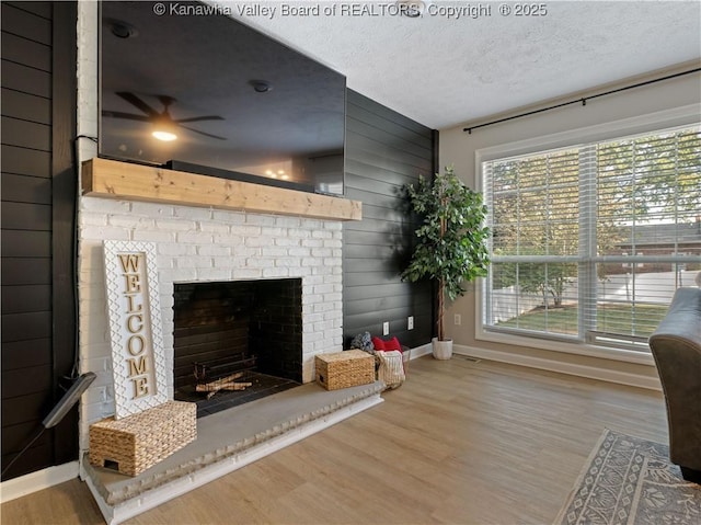 living room with ceiling fan, a brick fireplace, a textured ceiling, wooden walls, and hardwood / wood-style flooring