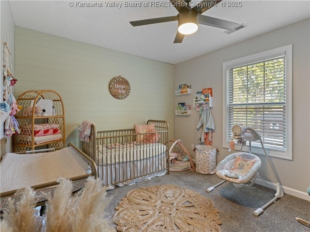 carpeted bedroom featuring a nursery area and ceiling fan