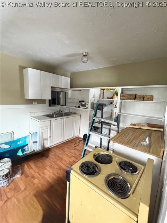 kitchen with light wood-type flooring, white cabinetry, electric range, and sink