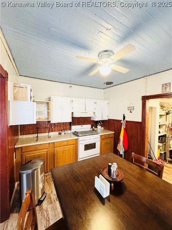 kitchen with white cabinets, wooden walls, ceiling fan, light hardwood / wood-style flooring, and white range