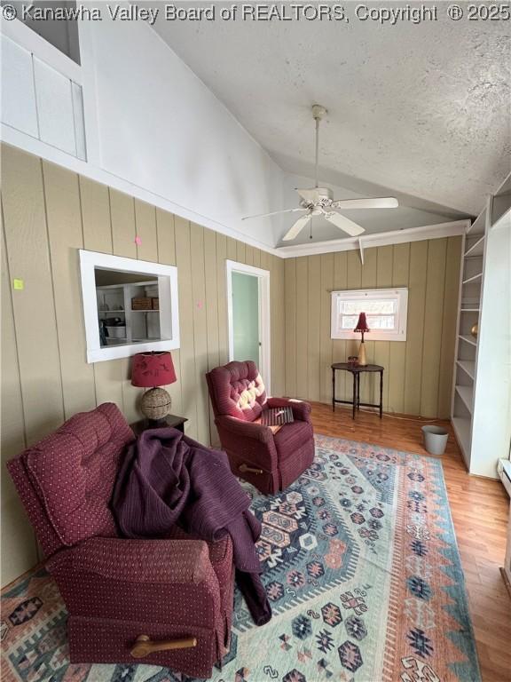 living room with a textured ceiling, hardwood / wood-style floors, wood walls, vaulted ceiling, and ceiling fan