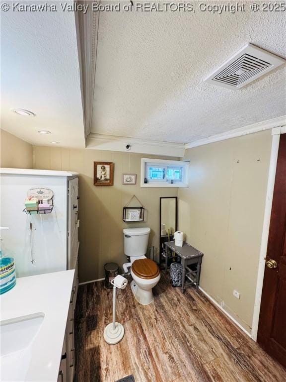 bathroom with toilet, wood-type flooring, a textured ceiling, ornamental molding, and vanity