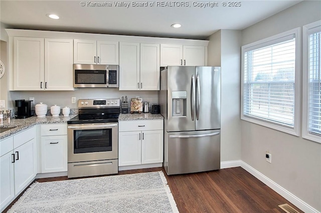 kitchen with appliances with stainless steel finishes, a healthy amount of sunlight, white cabinets, and light stone counters