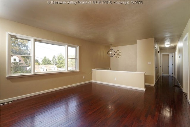 empty room with dark hardwood / wood-style flooring and a chandelier