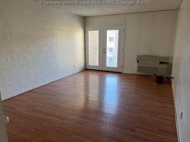 spare room with brick wall, french doors, and dark wood-type flooring