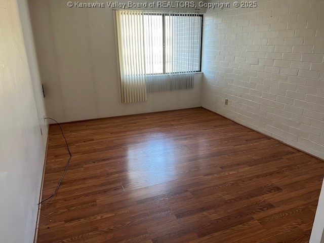 empty room with brick wall and dark wood-type flooring