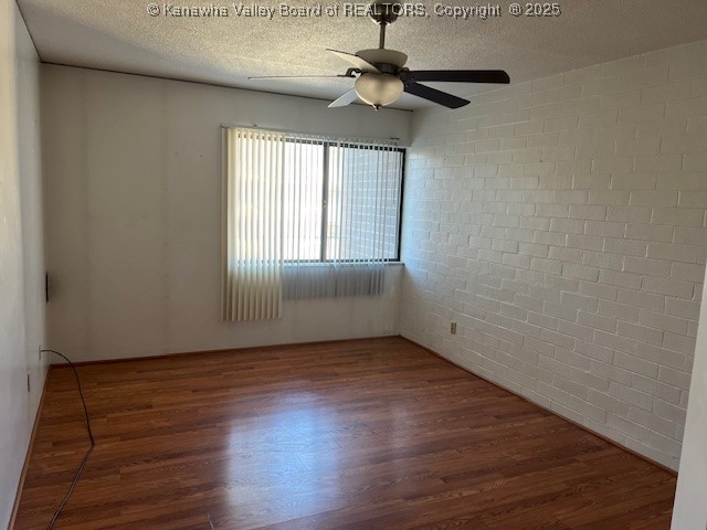 empty room with brick wall, dark hardwood / wood-style flooring, a textured ceiling, and ceiling fan