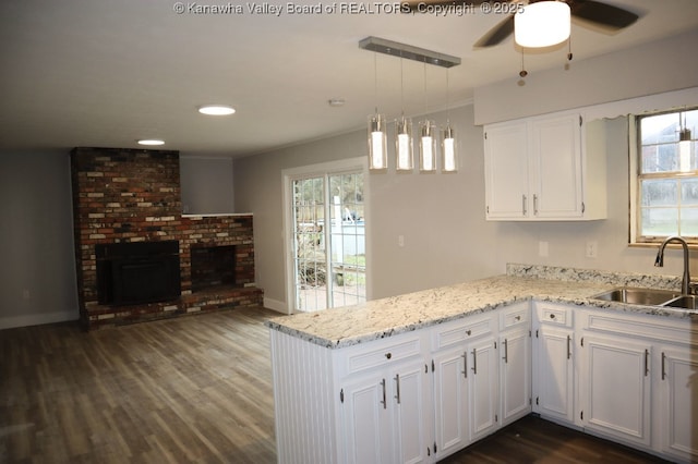 kitchen with hanging light fixtures, kitchen peninsula, a fireplace, sink, and white cabinetry