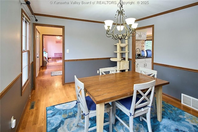 dining room featuring sink, a chandelier, ornamental molding, and light wood-type flooring