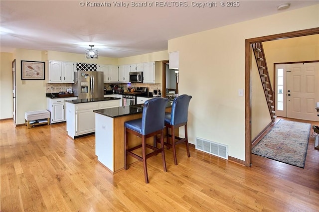 kitchen featuring stainless steel appliances, a breakfast bar, tasteful backsplash, light wood-type flooring, and white cabinets