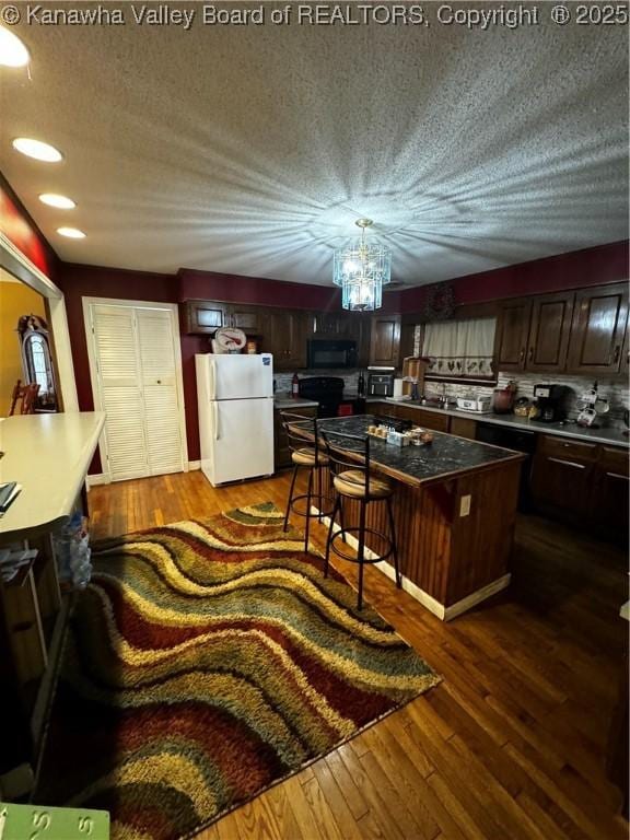 kitchen featuring dark hardwood / wood-style floors, a kitchen bar, a kitchen island, white refrigerator, and dark brown cabinetry