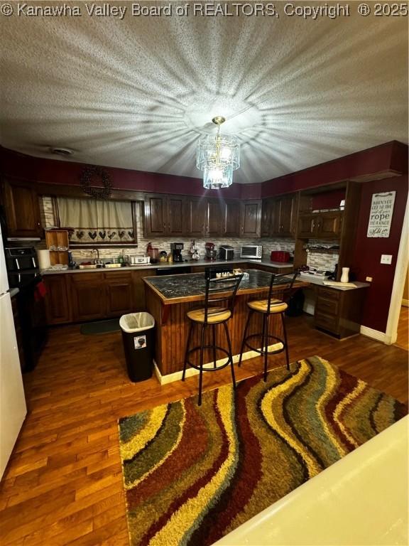 kitchen with a kitchen island, dark hardwood / wood-style floors, dark brown cabinets, and a breakfast bar area