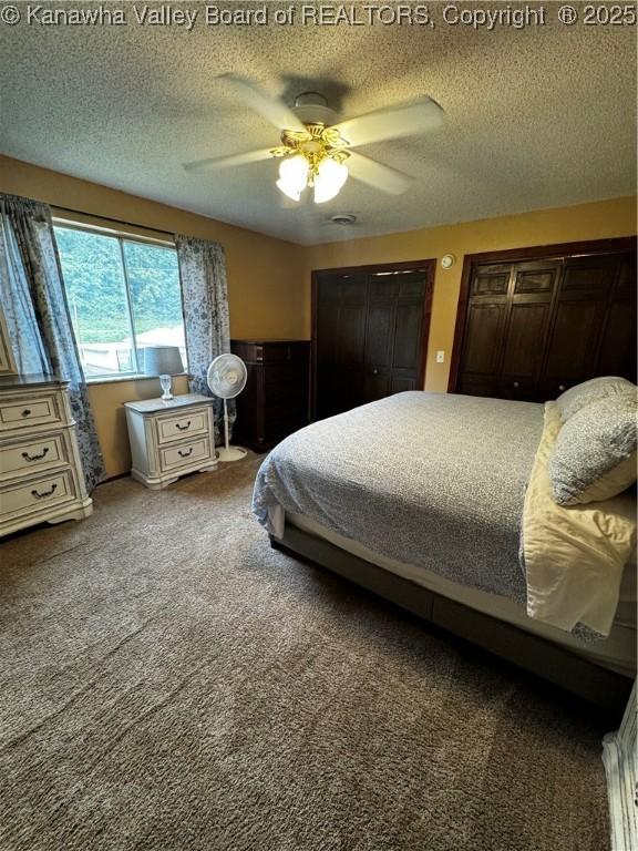 bedroom featuring a textured ceiling, ceiling fan, carpet, and multiple closets