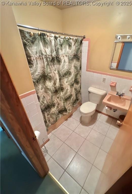 bathroom with toilet, walk in shower, tile walls, tile patterned floors, and sink