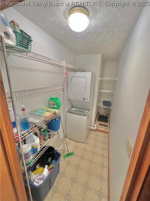 washroom with a textured ceiling and stacked washer / drying machine