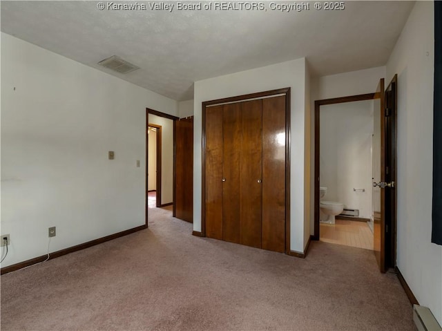 unfurnished bedroom with light carpet, a baseboard heating unit, a closet, and ensuite bathroom